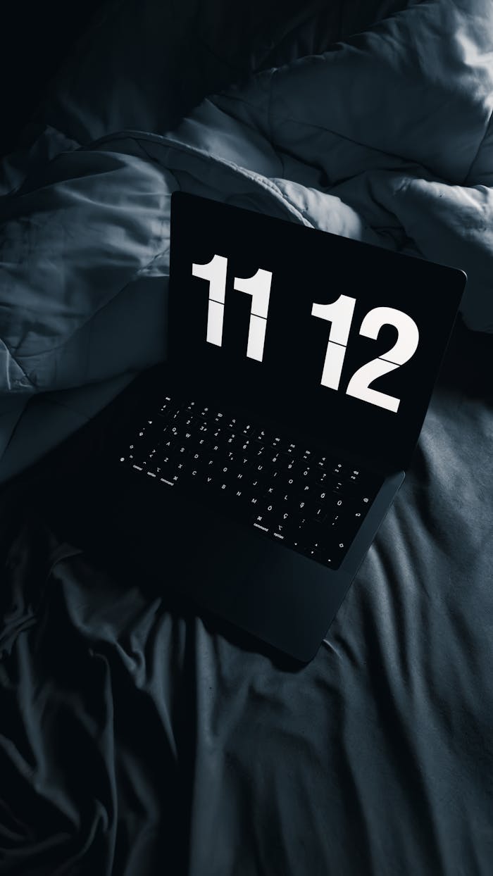 Laptop with digital clock display resting on a bed in low light, showcasing nighttime ambiance.