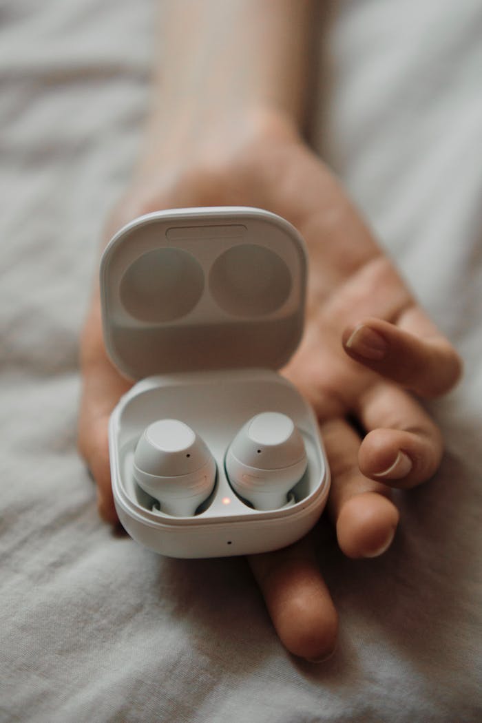 Compact wireless earbuds resting in an open case, held by an adult hand.
