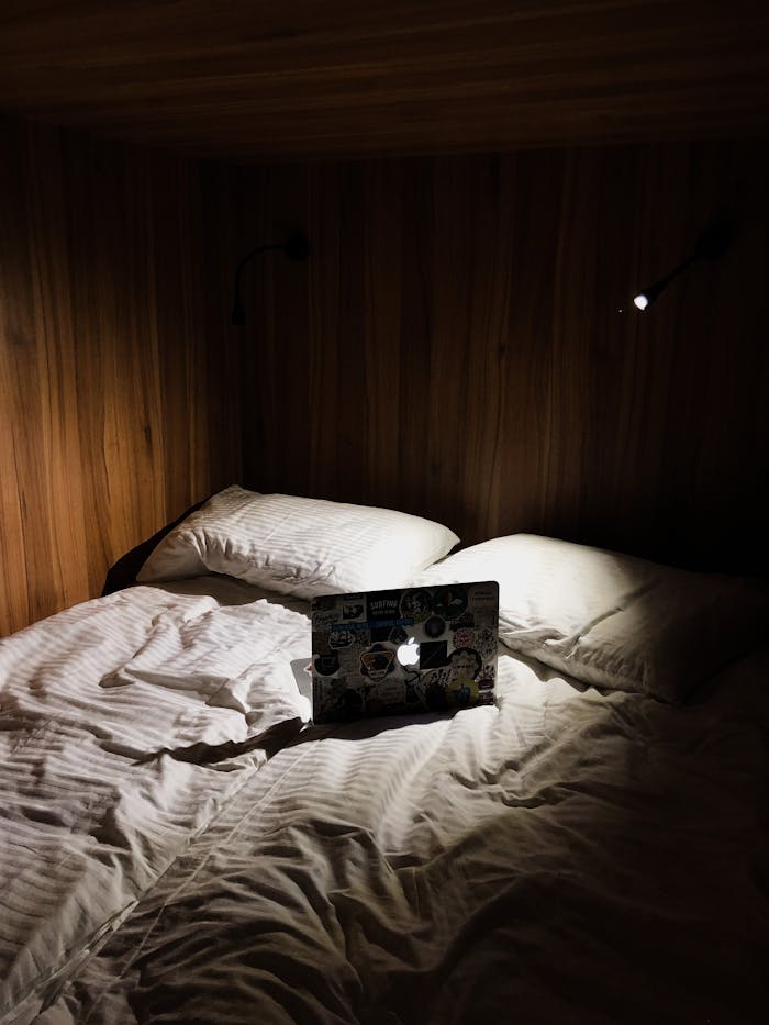 A cozy wooden bedroom featuring a well-lit laptop on a bed with pillows and blanket.